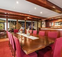A dining room in a family house with wooden elements and red chairs at the table.
