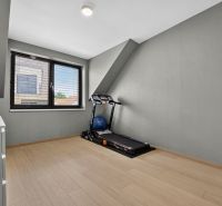 A room with a treadmill, wooden decor flooring, gray walls, window.