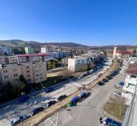 A street with cars and apartment buildings, surrounded by hills in Brezová pod Bradlom.