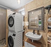 A bathroom in a family house with a shower, a washing machine, a dryer, and shelves with towels.