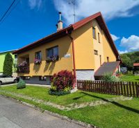 A family house in Podolínec with a garden and a yellow facade, surrounded by greenery.