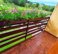 A balcony of a family house in Podolínec with flowers and a view of greenery.