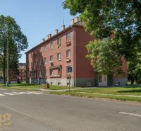 Brick apartment building with three floors in Poprad surrounded by greenery and a bench.
