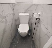 A toilet in a 3-room apartment with marble tiles on the walls.