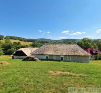 A family house in Dobroč surrounded by meadows and hills under a blue sky.