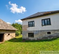 A family house in Dobroč with a concrete facade and a wooden shed in a green garden.