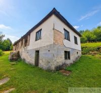 A family house in Dobroč with a damaged facade, built on a grassy slope.