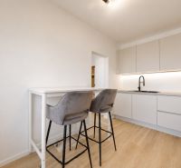 A kitchen with bar seating, wooden decor flooring, and white cabinets in a three-room apartment.