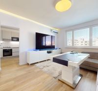 Living room with a large television and a kitchenette, 3-room apartment with a wooden decor floor.