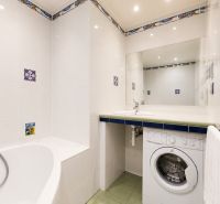 A bathroom with a bathtub, washing machine, and white tiles in a 3-room apartment.