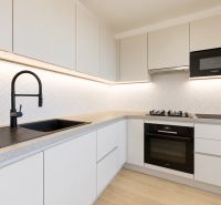 A modern kitchen in a 3-room apartment with white cabinets, a black sink, and a range hood.