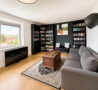 Living room in a 3-room apartment with a sofa, bookshelf, wood-patterned floor, and a large window.