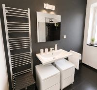 A bathroom in a 3-room apartment with a dark wall, a large mirror, and light furniture.