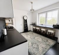 A kitchen in a 3-room apartment with a bar counter, dark countertops, and a large window.