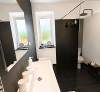 Bathroom in a 3-room apartment with black tiles, a shower corner, and a white sink.