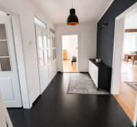 A hallway in a 3-room apartment with light walls, a black chandelier, and a dark floor.