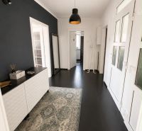 The hallway of a 3-room apartment with dark tiles and a carpet, complemented by wall lighting.
