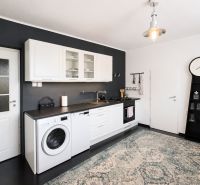 A kitchen in a 3-room apartment with a black wall, white cabinets, and a carpet.