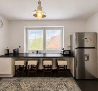 A kitchen in a 3-room apartment with a refrigerator, a bar counter, and four chairs.