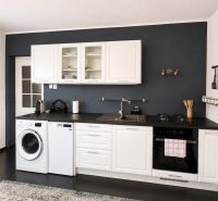 A kitchen in a 3-room apartment with a dark wall, white cabinets, and appliances.