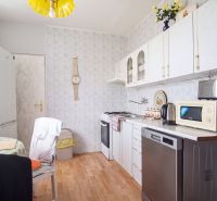 A kitchen in a 4-room apartment with a wooden decor floor and white cabinets.