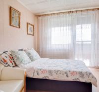 A bedroom in a 4-room apartment with decorative pillows and sheer curtains on the window.