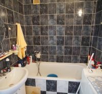 A bathroom in a 4-room apartment with a bathtub and darker tiles.