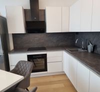 A kitchen in a 2-room apartment with white cabinets, a dark countertop, and a floor with a wood decor.