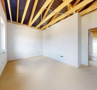 A room in a family house with a wooden decor floor and an unplastered ceiling.