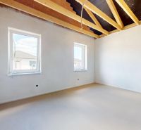 An unfinished interior with a concrete floor and wooden beam ceiling in a family house.