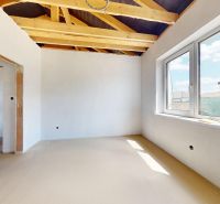 A room in a family house with a wooden beam ceiling and a large window.