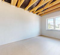 A room in a family house with white walls, ceiling beams, and a view from the window.