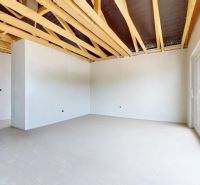 A spacious room in a family house with light walls and an exposed ceiling.