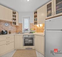 A kitchen in a cottage with light cabinets and an orange backsplash behind the sink.