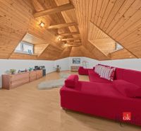 The attic of a cottage with a red sofa, wooden paneling, and a wooden-patterned floor.