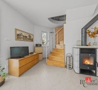 Interior of a cottage with a tiled stove, a television, and a wooden staircase.