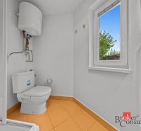 A bathroom with a window and a boiler, flooring with an orange design in a cottage.