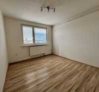 A room in a 3-bedroom apartment with a large window and a wooden decor floor.