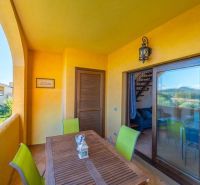Terrace of a recreational apartment in Sardinia with a wooden table and colorful chairs.