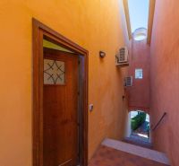 The hallway of a holiday apartment in Sardinia with colorful plastered walls and wooden doors.