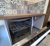 An open dishwasher in a 3-room apartment with mosaic tiles and wooden decor.