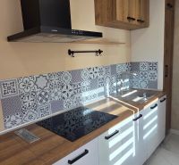 A kitchen with white cabinets, a wooden decor floor, decorative tiles.