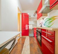 A kitchen in a 3-room apartment with vibrant red cabinets and a wood-patterned floor.