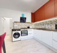 A kitchen in a 2-room apartment with colorful tiles, red cabinets, and a wooden-patterned floor.