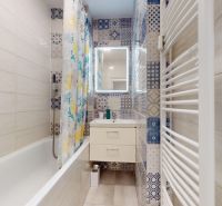A bathroom with a bathtub, patterned tiles, and a mirror in a 2-room apartment.