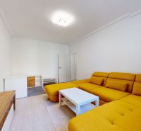 Living room of a two-room apartment with a yellow sofa and a white table.