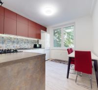 A kitchen in a 2-room apartment with colorful tiles, red cabinets, and a wood-patterned floor.