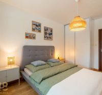 A bright bedroom with a bed, wood-patterned flooring, and a wardrobe in a two-room apartment.