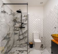 Bathroom with tiles and a glass shower enclosure in a 2-room apartment.