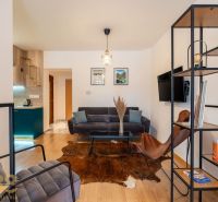 A room in a 2-room apartment with a sofa, armchairs, a shelf, and a floor with a wooden decor.